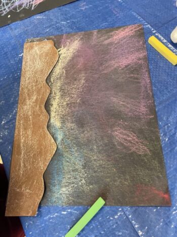 A child's colored in paper of the Northern Lights. It has reds, pinks, blues, greens, and yellows colored on black paper.